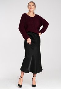 Burgundowa, puszysta sweter z szerokim dekoltem, w połączeniu z gładką, czarną satynową spódnicą midi i czarnymi sandałami na kostkę.