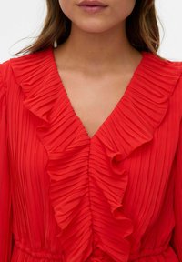 Abito plissettato rosso con scollatura a V profonda e dettagli in volant, tessuto morbido e vita elasticizzata per una vestibilità perfetta.