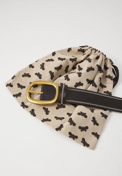 Sacchetto di tessuto beige con motivo a farfalla nero, stretto con una cintura in pelle nera dotata di una fibbia rettangolare dorata e cuciture bianche.