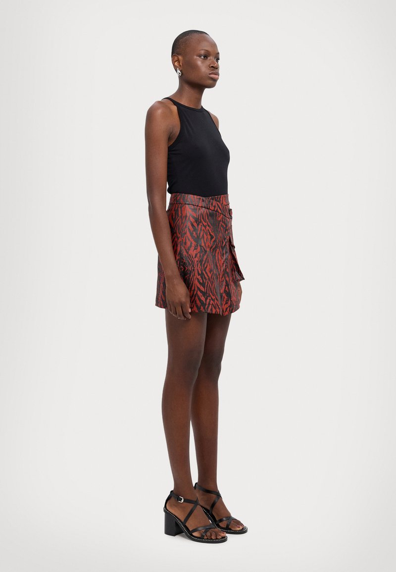 Haut sans manches noir, jupe rouge et noire à motif avec un design portefeuille, et sandales noires à lanières avec un talon carré.