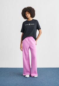 Μαύρο βαμβακερό t-shirt με λογότυπο "Nike Shox", σε συνδυασμό με φαρδιά ροζ φόρμα με κορδόνι και λευκά λογότυπα.