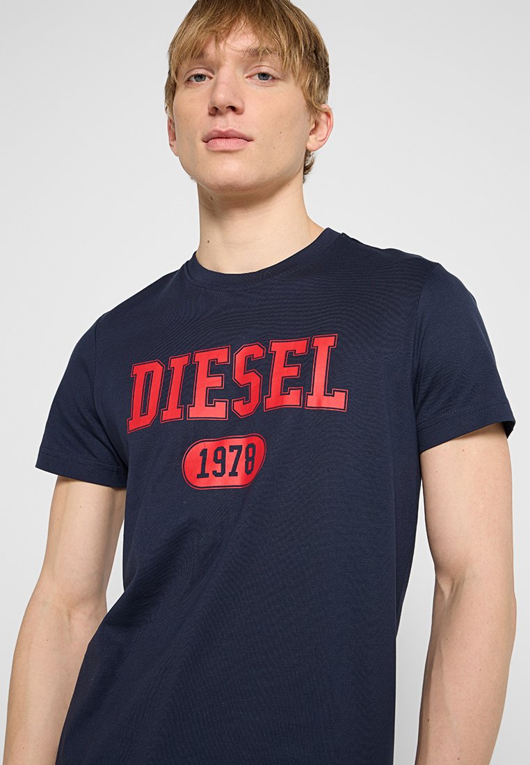 Navyblauwe katoenen t-shirt met vet rood "DIESEL" tekst en "1978" in een afgeronde witte badge, ronde nek en korte mouwen.