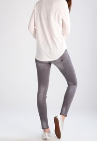 Slim-fit šedé džíny s vybledlým vzhledem a designem pěti kapes, doplněné světle šedým topem s dlouhým rukávem a bílými teniskami.