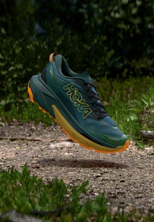 Chaussure de course verte avec accents noirs et semelle extérieure orange. Caractérisée par une tige en mesh respirant, un design de soutien, et un logo "HOKA" bien visible.