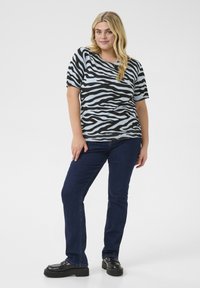 Čierne a svetlomodré tričko so zebra pruhmi a krátkymi rukávmi, spárované s tmavomodrými džínsy a čiernymi platformovými topánkami. Jednoduchý a neformálny dizajn.