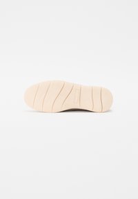 Sål af sko, gummimateriale, lys farve, tekstureret med riller, logo prægede, glatte kanter, designet til greb og komfort.