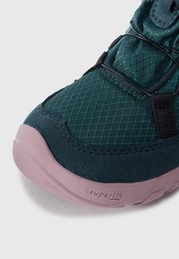 Tomaia in tessuto verde con motivo a diamante, dettagli in suede teal scuro a contrasto e suola in gomma rosa con marchio "superfit".