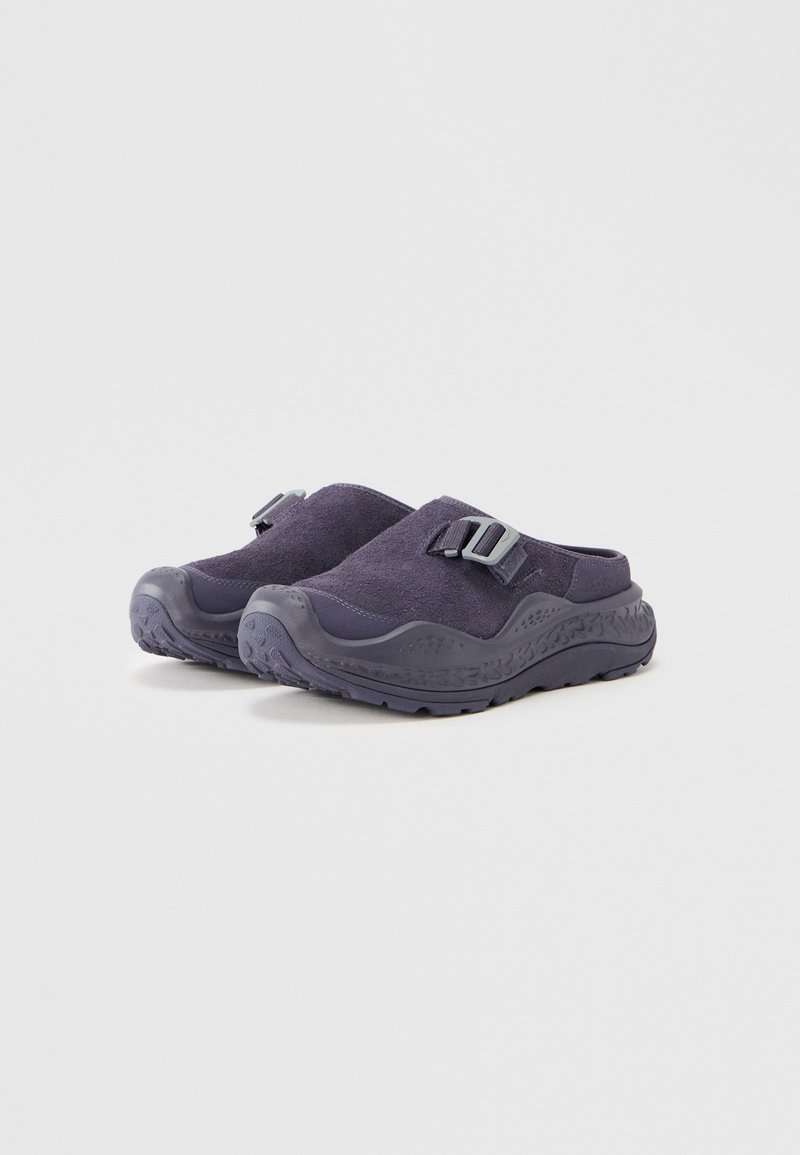 Zuecos azul marino hechos de tela suave con una superficie texturizada, que cuentan con una suela de goma y una correa ajustable con detalle de hebilla.