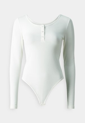Body alb cu mânecă lungă, realizat dintr-un material elastic, cu un decolteu rotund și o panglică cu trei nasturi în față.