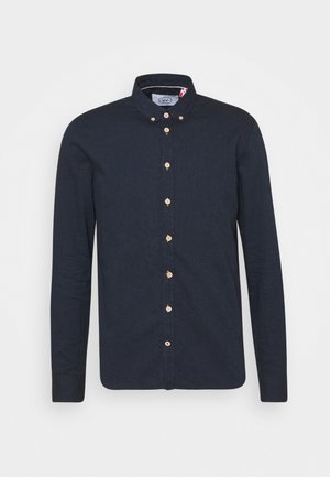 Camicia a maniche lunghe di colore blu scuro realizzata in tessuto dalla trama liscia, con colletto alla coreana e bottoni chiari sulla parte anteriore.