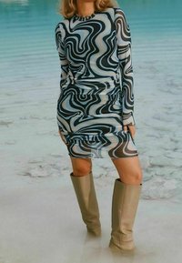 Robe à manches longues en tissu transparent avec un motif ondulé noir, beige et bleu. Associée à des bottes beiges montantes jusqu'aux genoux. Texture douce.