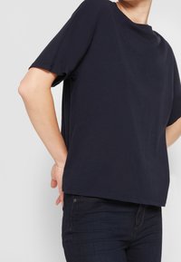 Camiseta de algodón azul marino de manga corta, con corte relajado y cuello redondo, combinada con jeans oscuros. Textura suave, diseño sencillo.