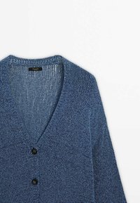 Blå stickad kofta med V-ringning och två svarta knappar på en vit bakgrund, som visar det detaljerade texturerade tyget.