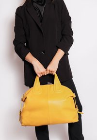 Borsa a tracolla gialla in pelle con superficie texture, forma arrotondata e doppie maniglie a punta. Presenta una chiusura con zip e accenti decorativi laterali.