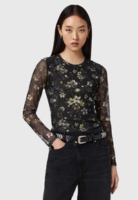 Μαύρο μακρυμάνικο τοπ από διαφανές ύφασμα με λουλουδάτο σχέδιο σε πράσινο και κίτρινο, σε συνδυασμό με  μαύρο τζιν ψηλόμεσο και μαύρη ζώνη.