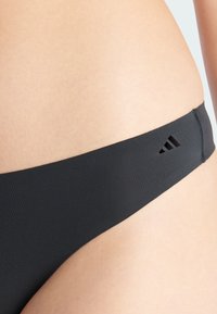Svart bikiniunderdel gjord av mjukt tyg, med en låg midja och en liten utskärning med Adidas-logotypen på midjebandet.