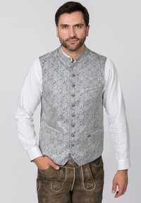 Blaues Paisley-Muster-Weste mit Stehkragen, Knöpfen auf der Vorderseite und zwei Taschen, getragen über einem weißen Hemd. Braune Hosen runden den Look ab.