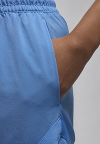 Blå sportsshorts med elastisk talje, glat tekstur og en sidelomme med en dekorativ detalje nær kanten.