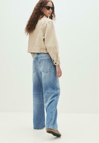 Beige denim takki, rento malli, nappiyksityiskohdilla. Vaaleansiniset leveälahkeiset farkut, kuluneet yksityiskohdat. Ruskeat liuku-kengät, pyöreä kärki.