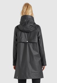 Černá, voděodolná bunda s kapucí, střední délky, hladké textury a s patentním uzávěrem vzadu pro ventilaci.
