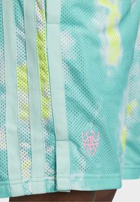 Pantalones cortos de malla turquesa con patrones amarillos y blancos, que cuentan con tres franjas verticales y un logo rosa en el dobladillo.