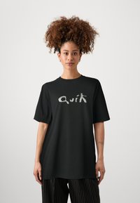 Svart oversized t-shirt med en silverfärgad grafisk textlogo "Quik." Tillverkad av mjukt tyg, med korta ärmar och en klassisk rundad halsringning.