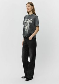 T-shirt grafico grigio con maniche corte, caratterizzato da un design bianco. Jeans in denim nero con vestibilità ampia e decorazioni sparse sull'orlo.