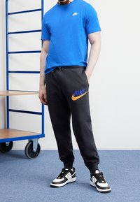Blå bomullströja, svarta sweatpants med orange och blå Nike-logotyp, kombinerat med svarta och vita sneakers. Enkelt design, avslappnad passform.
