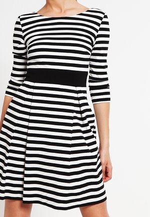 Robe rayée horizontale noir et blanc avec manches trois-quarts et ceinture noire unie, portée par une personne debout.