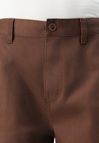 Braune Hosen aus glattem Stoff, mit einem einzelnen Knopfverschluss an der Taille, Gürtelschlaufen und standardmäßigen Vorderentaschen.