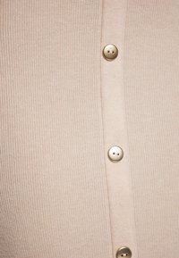 Cardigan a coste beige con una fila di bottoni rotondi dorati lungo la parte anteriore, che offre un aspetto texturizzato e strutturato.