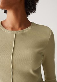 Rippenshirt mit langen Ärmeln in Hellgrün, mit rundem Halsausschnitt und einer Vordernaht-Detail. Weicher, strukturierter Stoff mit dezenten Nähten.