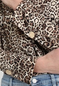 Leopardprint bluse i et blødt stof med en knapmanchet i guldtoner. Designet inkluderer forskellige nuancer af brun og sort.