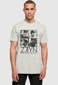 Tejfehér pamut póló, fekete grafikai képekkel és "ZAYN ROOM UNDER THE STAIRS" felirattal. Klasszikus szabású, rövid ujjú és bordázott nyakkivágással.