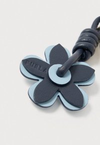 Μπρελόκ λουλουδιού από δέρμα σε σκούρο μπλε και ανοιχτό μπλε, με στρωμένα πέταλα και στρογγυλό κέντρο. Σφραγισμένο με τη λέξη "Furla" στο στρώμα του σκούρου μπλε.