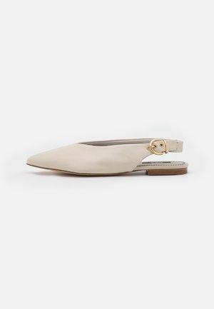 Beige spids tå flad slingback sko med spænde i guld på en lav træhæl, vist på hvid baggrund.