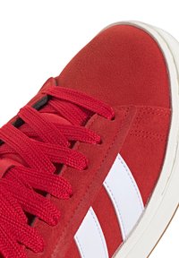 Rote Wildleder-Sneaker mit weißen Lederstreifen, strukturierten roten Schnürsenkeln und einer weißen Gummisohle mit einer Gummisohle. Nahaufnahme.