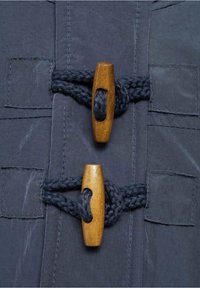 Détail d'un manteau en tissu marine avec deux fermetures à bascule en bois, accompagnées d'une corde marine tressée et de surpiqûres visibles.