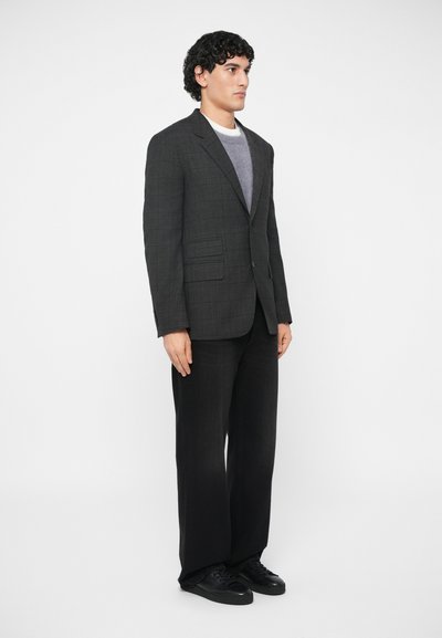 Gray plaid blazer with two front pockets over a gray sweater, paired with black wide-leg pants and black sneakers, set against a white background.