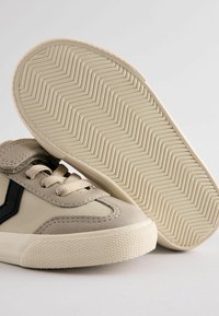 Beżowe sneakersy z czarnymi akcentami, z teksturowanej zamszowej i syntetycznej maty, wyposażone w sznurowanie oraz wzorzystą gumową podeszwę.