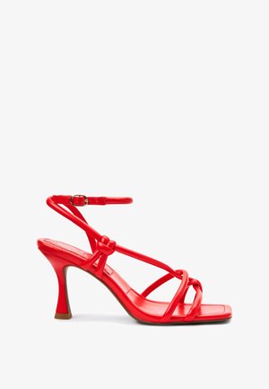 Sandalia roja de tacón alto con diseño de tiras y detalle anudado. Material sintético suave, puntera cuadrada y tacón cónico de color contrastante.