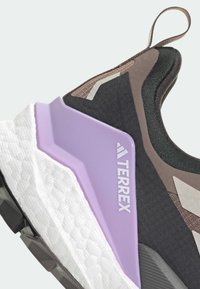 Melna sporta apava ar pelēkiem, brūniem un violetiem akcentiem. Iezīmējas ar teksturētu audumu, baltu polsterētu starpzoli un izteiksmīgu logotipu sānos.