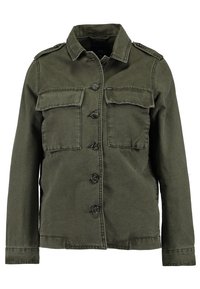 Kurtka w kolorze oliwkowej zieleni wykonana z bawełny, z przodu zapinana na guziki, z dwoma kieszeniami na piersiach oraz pagonami na ramionach. Długie rękawy z mankietami zapinanymi na guziki.