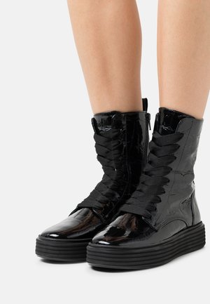 Bottines en cuir verni noir avec des semelles en caoutchouc épaisses, dotées d'un laçage à l'avant et d'une fermeture éclair sur le côté pour un enfilage facile.
