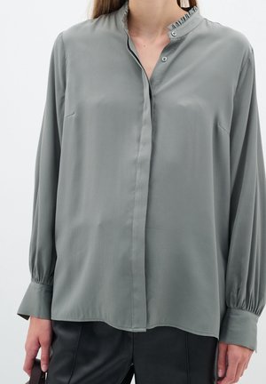 Camicia grigia a maniche lunghe in tessuto liscio, con colletto alla cinese e chiusura a bottoni, dotata di un lieve dettaglio arricciato all'escursione.