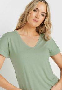 Jasnozielona krótka bluzka V-neck z krótkim rękawem, wykonana z miękkiego materiału, charakteryzująca się luźnym krojem i subtelną fakturą. Gładka powierzchnia bez wzorów.