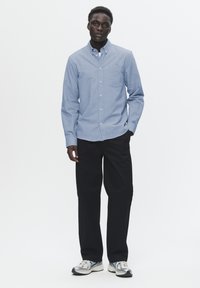 Light blue, button-up shirt with a collar and chest pocket, paired with black trousers and silver sneakers; smooth fabric, relaxed fit.
