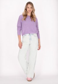 Pulover purpuriu pufos cu mâneci lungi, asortat cu blugi evazați decolorati. Modelul poartă pantofi roz cu talpă bej.