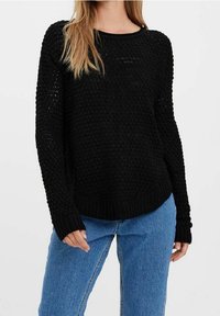 Maglione nero a maglia con un motivo testurizzato, scollo rotondo e orlo a coste. Maniche lunghe e vestibilità ampia, abbinato a jeans in denim blu.