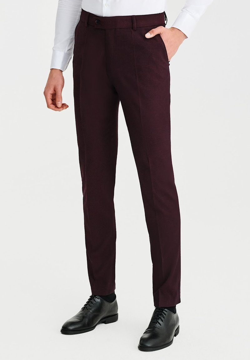 Burgundzkie spodnie wykonane z gładkiego materiału, slim fit, z paskami na pasek, pojedynczym zapięciem na guzik i bocznymi kieszeniami, w zestawie z czarnymi butami eleganckimi.